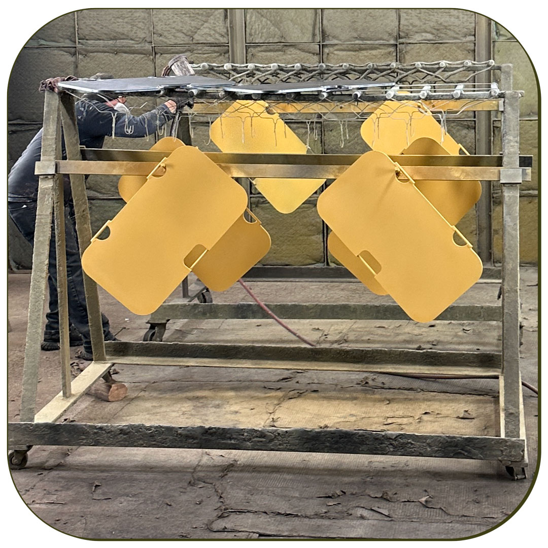 Photo of fabricated metal parts, painted yellow and hung up to dry